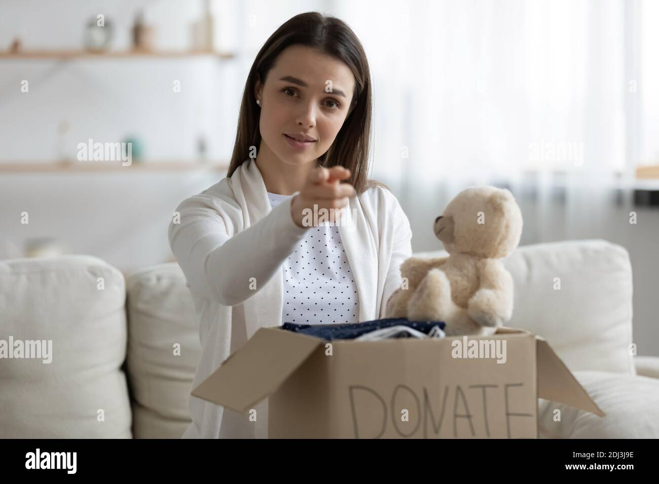 Young woman holding donation box, pointing finger at you Stock Photo