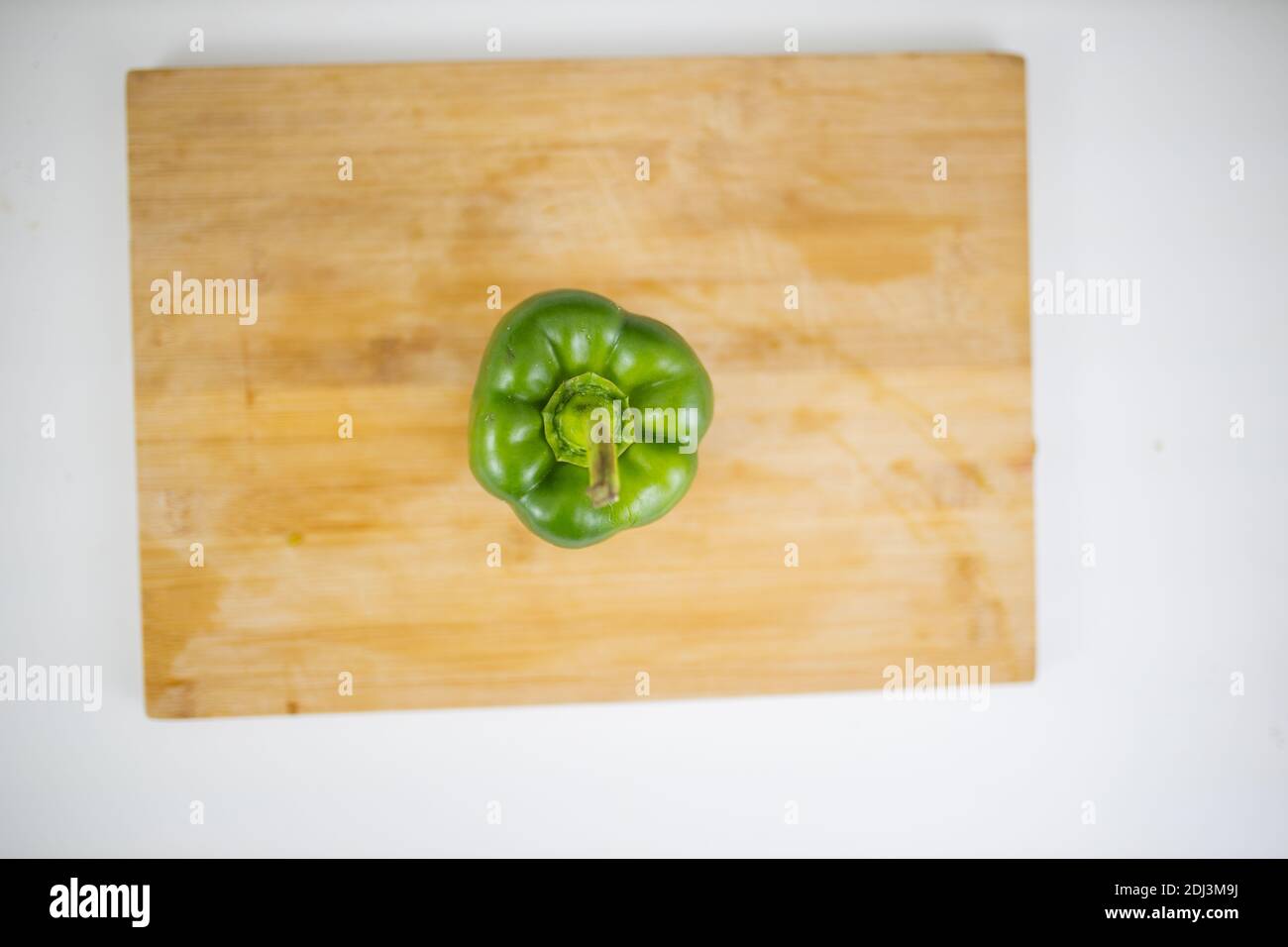 Green bell pepper on a cutting board above a white table Stock Photo ...