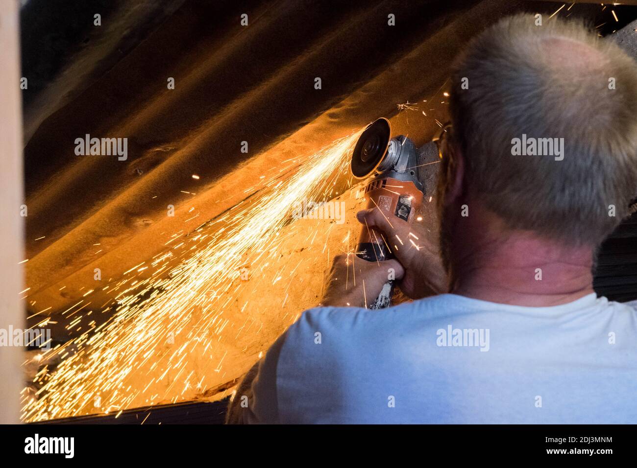 A man cutting metal roof with a flex radial saw with sparks flying Stock Photo