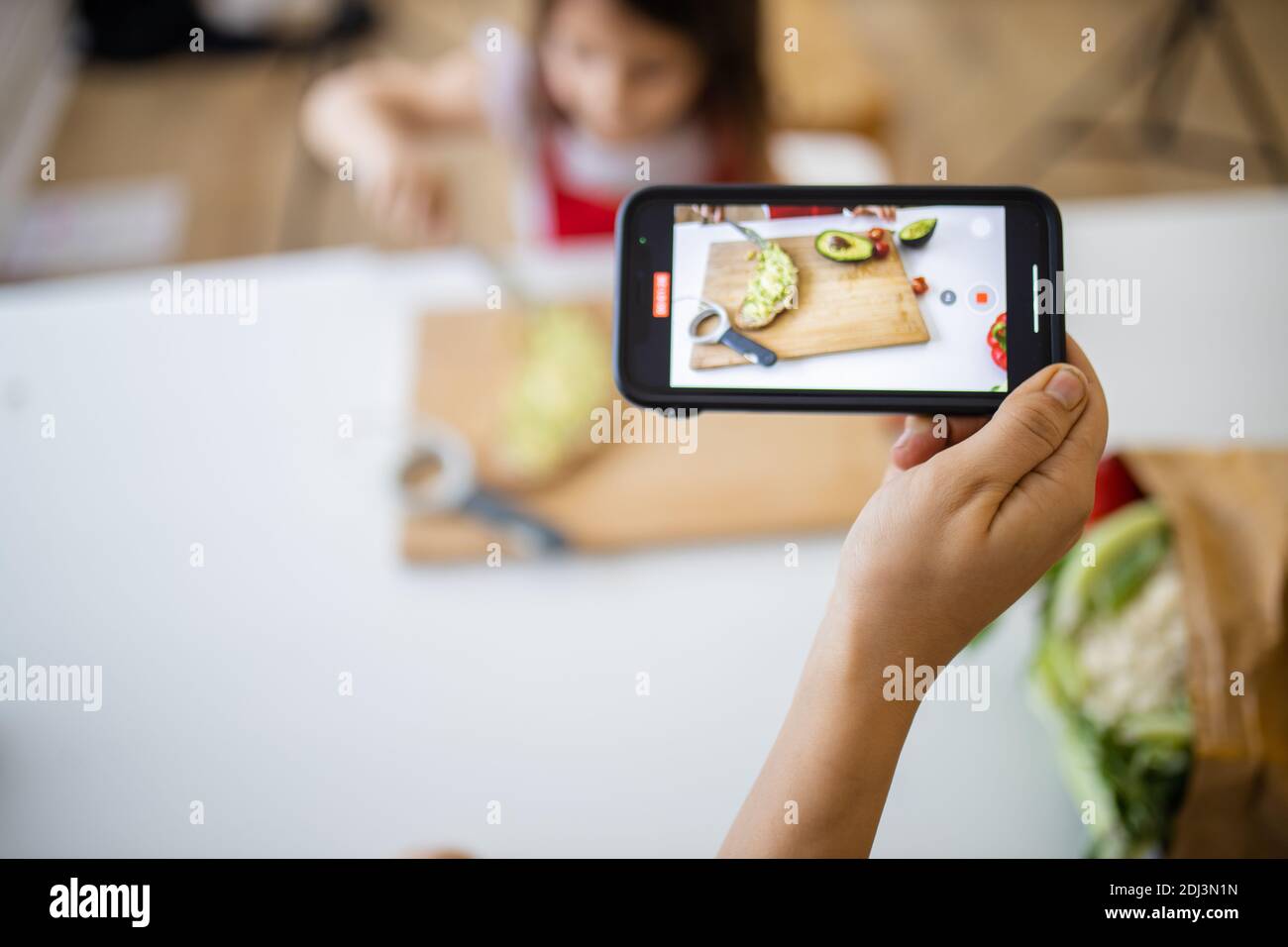 Female hand with a smartphone recording a little girl cutting an ...