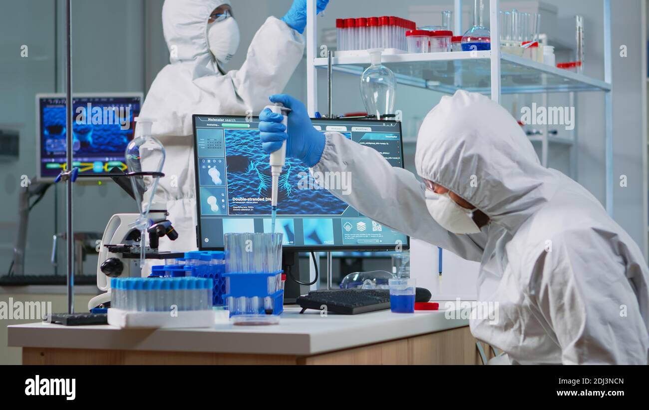 Research scientist in protection suit using micropipette filling test ...