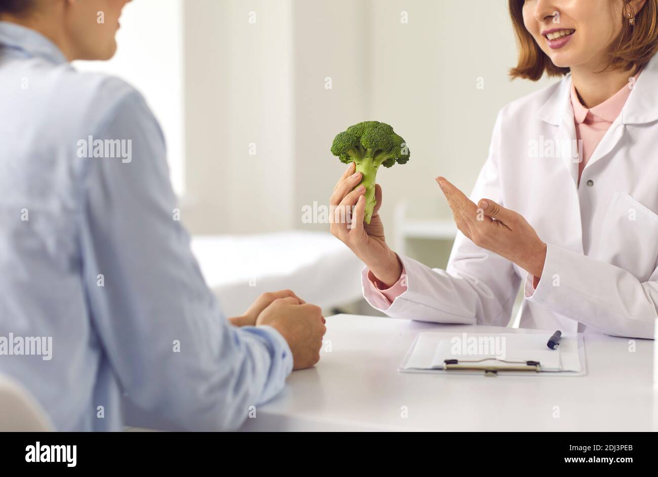 Nutritionist telling woman about benefits of healthy diet and recommending eating vegetables Stock Photo