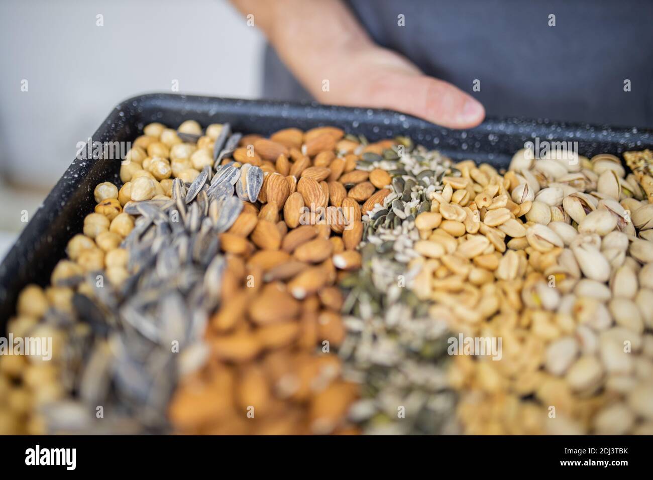 Male hands holding a black tray of nuts and seeds Stock Photo