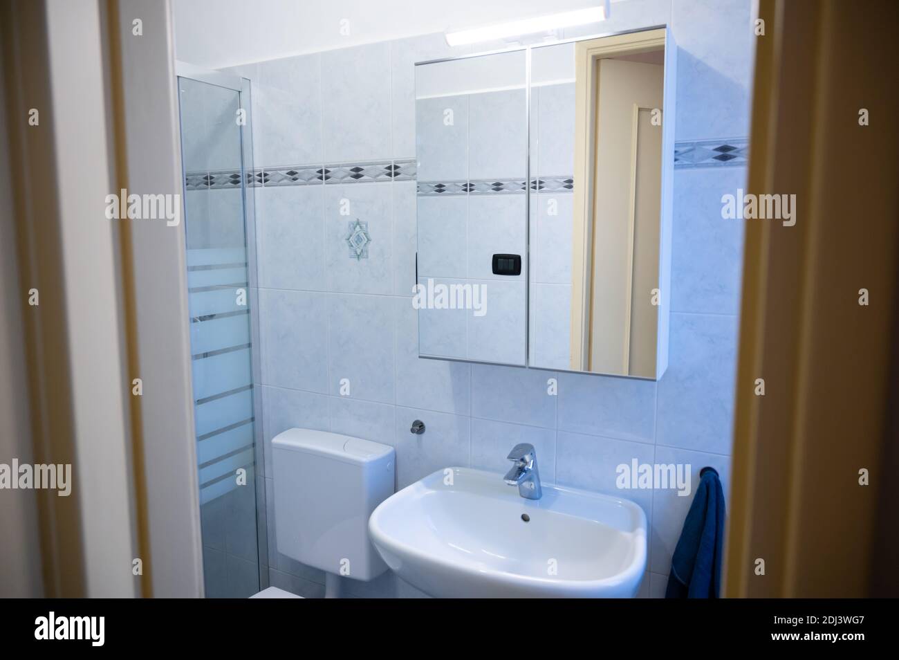 View of the interior of a bathroom from the entrance door. The yellow frame of the door is the frame: in evidence the mirror cabinet above the sink, o Stock Photo