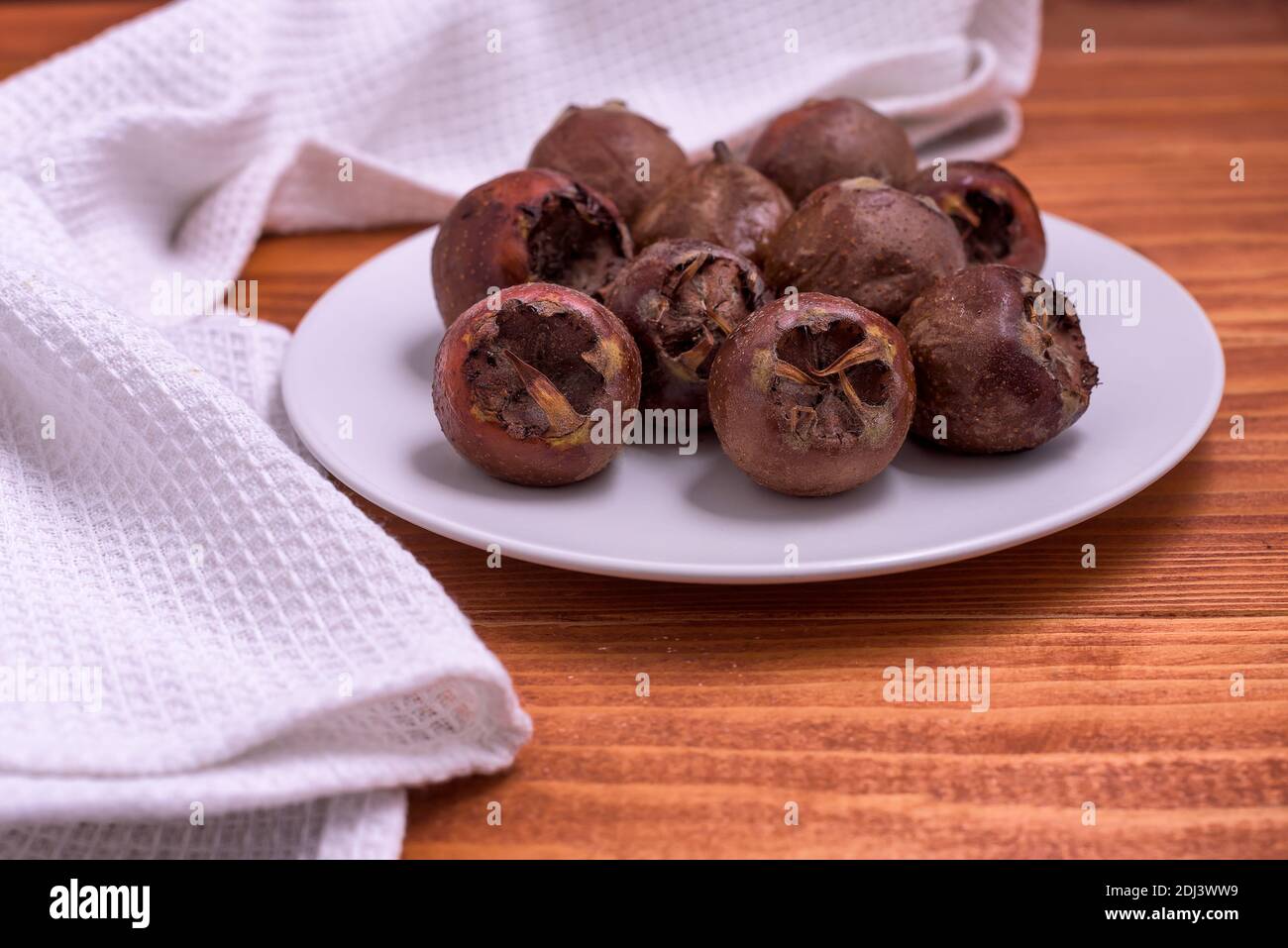 Fresh ripe organic common medlar fruit on a plate on wooden rustic background. Healthy food Mespilus germanica Stock Photo