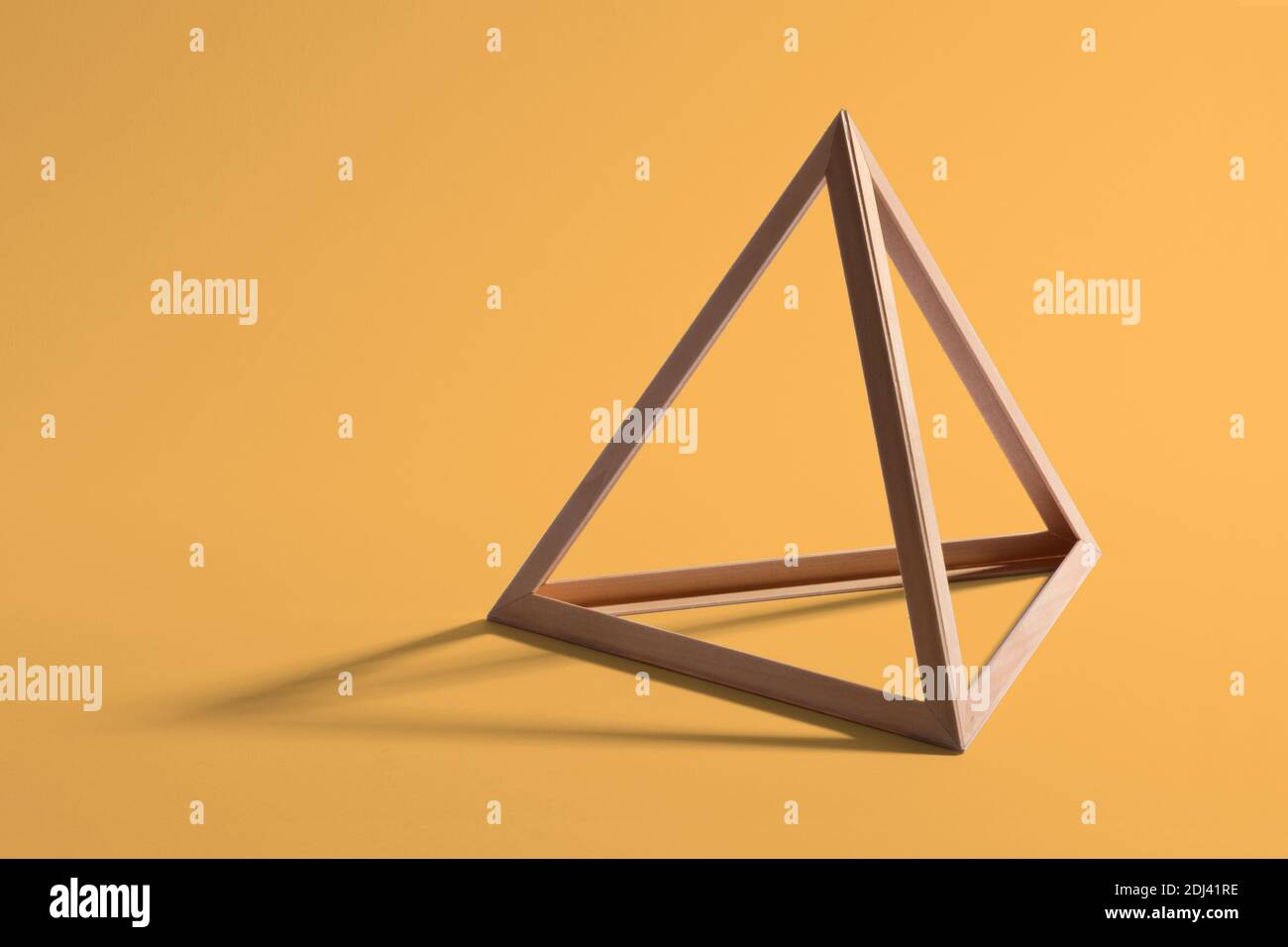 Open empty wooden triangular frame or pyramid shape forming a standard geometric triangle casting a shadow on a yellow background Stock Photo