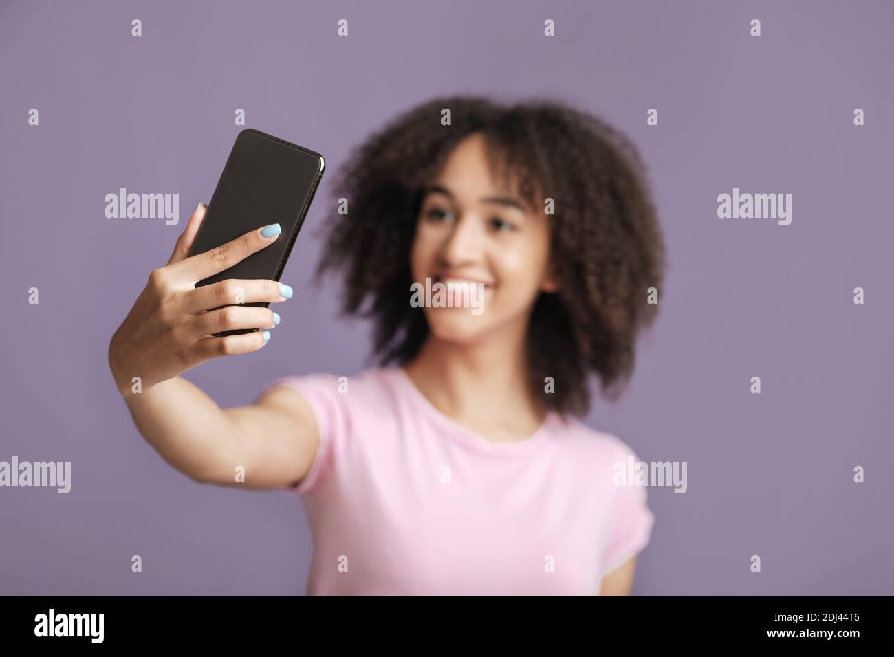 Happy lady makes selfie, focus on phone, isolated on violet background Stock Photo