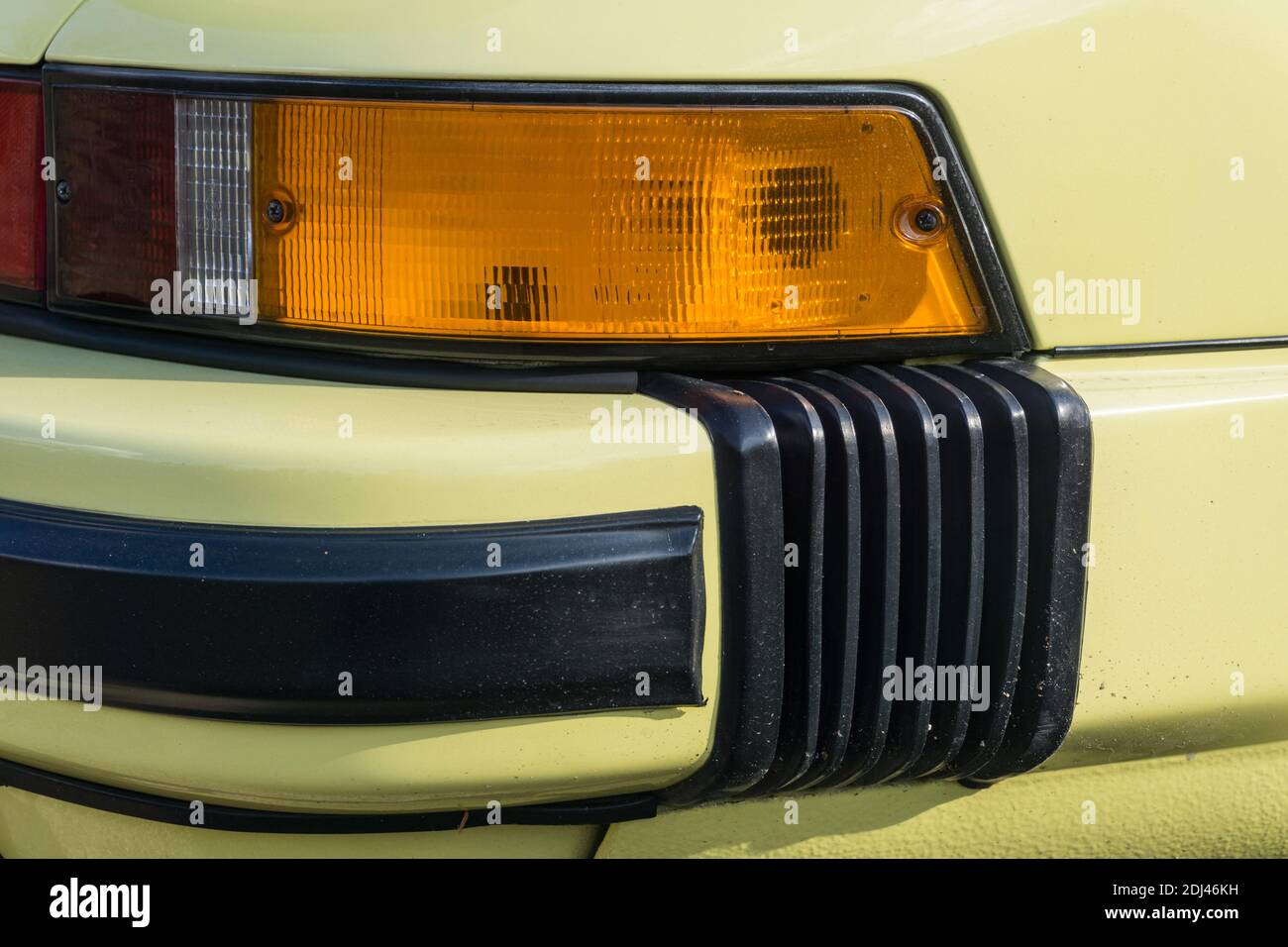 Close up detail of the rear bumper and indicator on a yellow eighties Porsche 911 3.2 Carrera sports car outside in sunshine. Stock Photo
