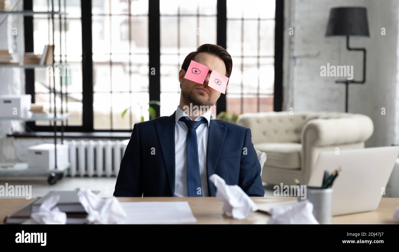 Tired sleepy businessman with stickers on eyes sleeping at workplace Stock Photo