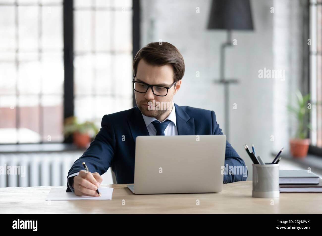 Confident businessman wearing glasses using laptop, writing notes Stock Photo