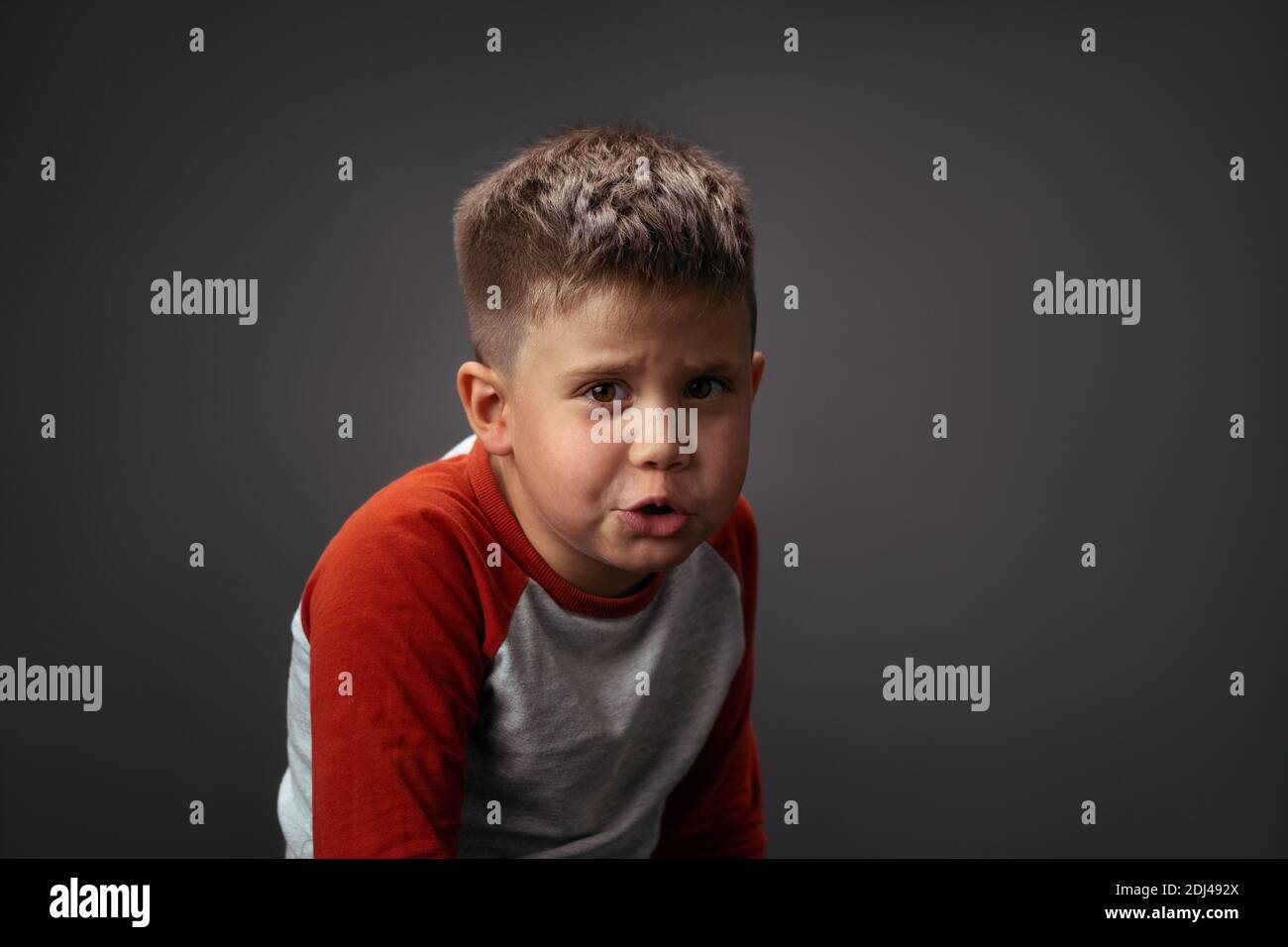 Cute little boy in red and white t-shirt posing on gray background. Facial expressions, emotions, feelings. Photo of a preschooler 6 years old on a Stock Photo