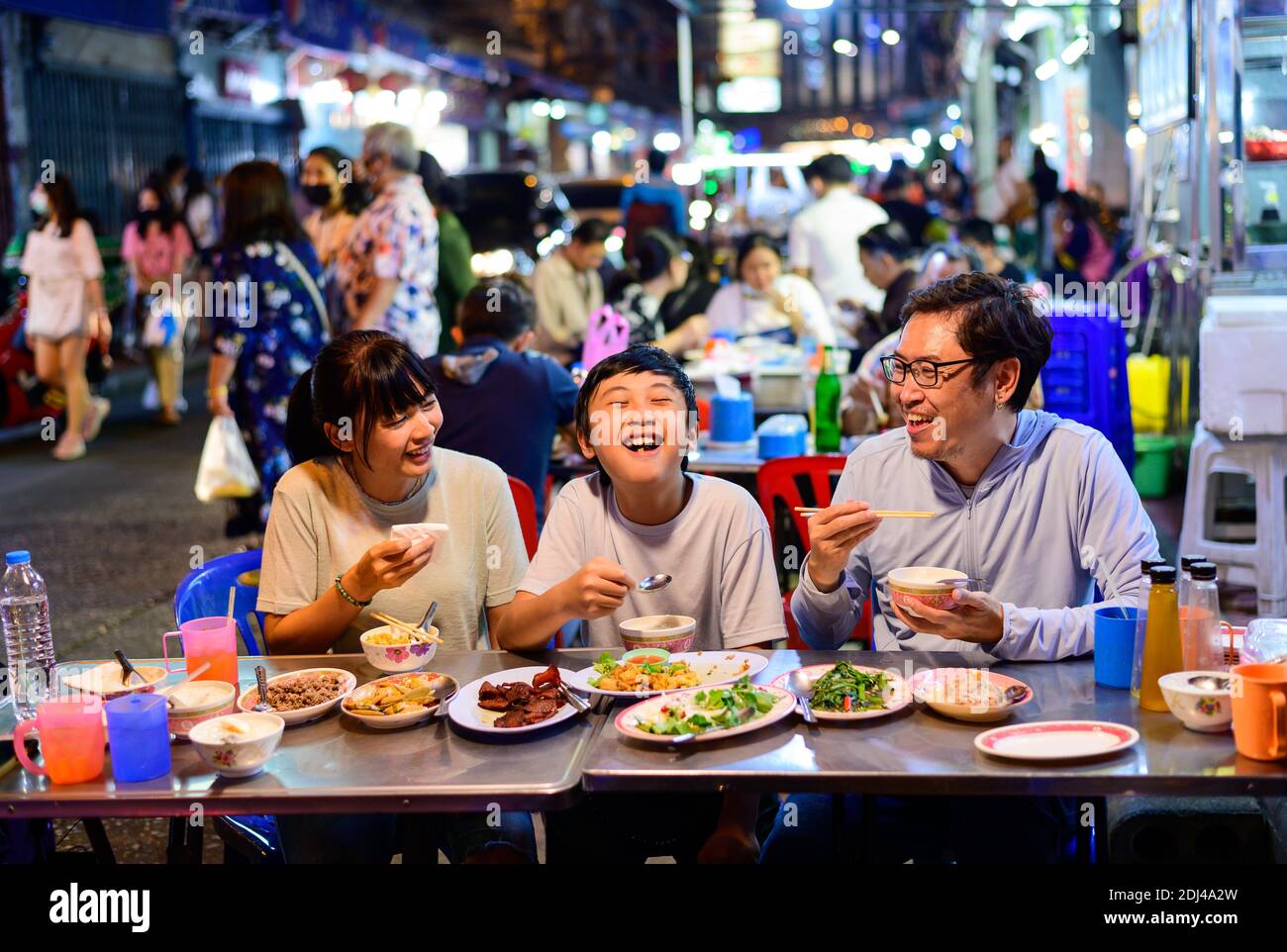 Asian family enjoy eating food on street food restaurant with crowd of