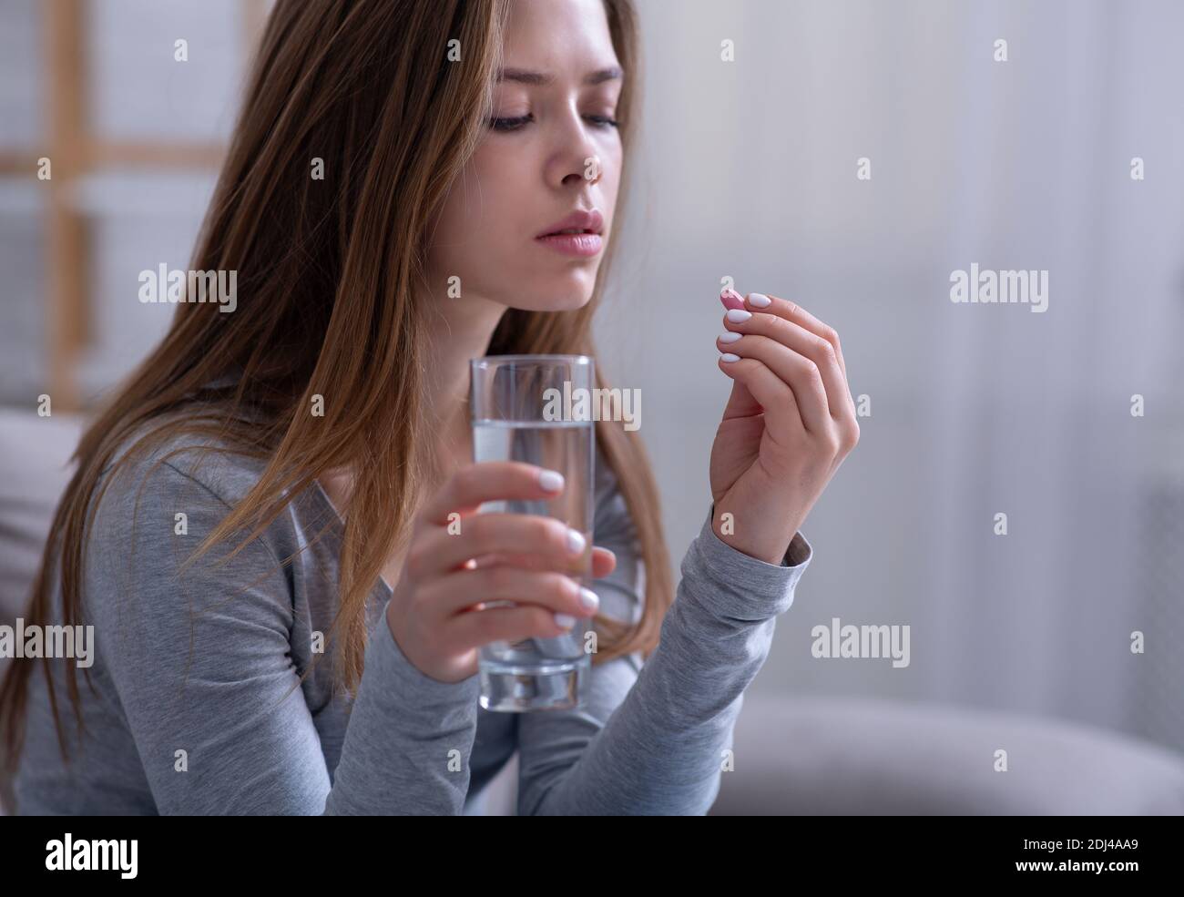 Treatment of depression. Unhappy young woman taking antidepressant, tranquilizer or sleeping pill at home, free space Stock Photo
