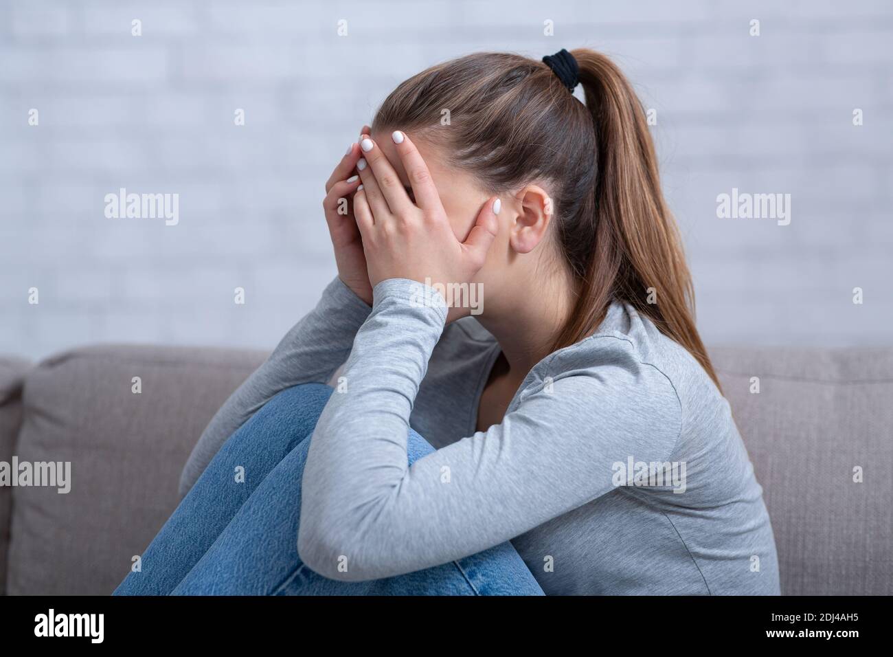 Side view of young woman with depression covering her face and crying on sofa at home Stock Photo