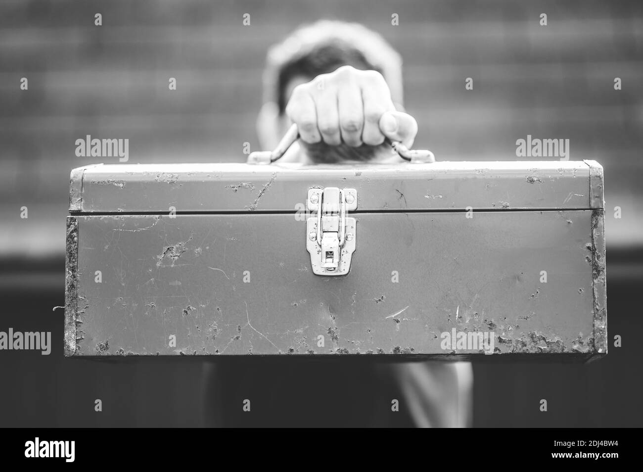 A greyscale shot of a male holding a toolbox in front of his face Stock Photo