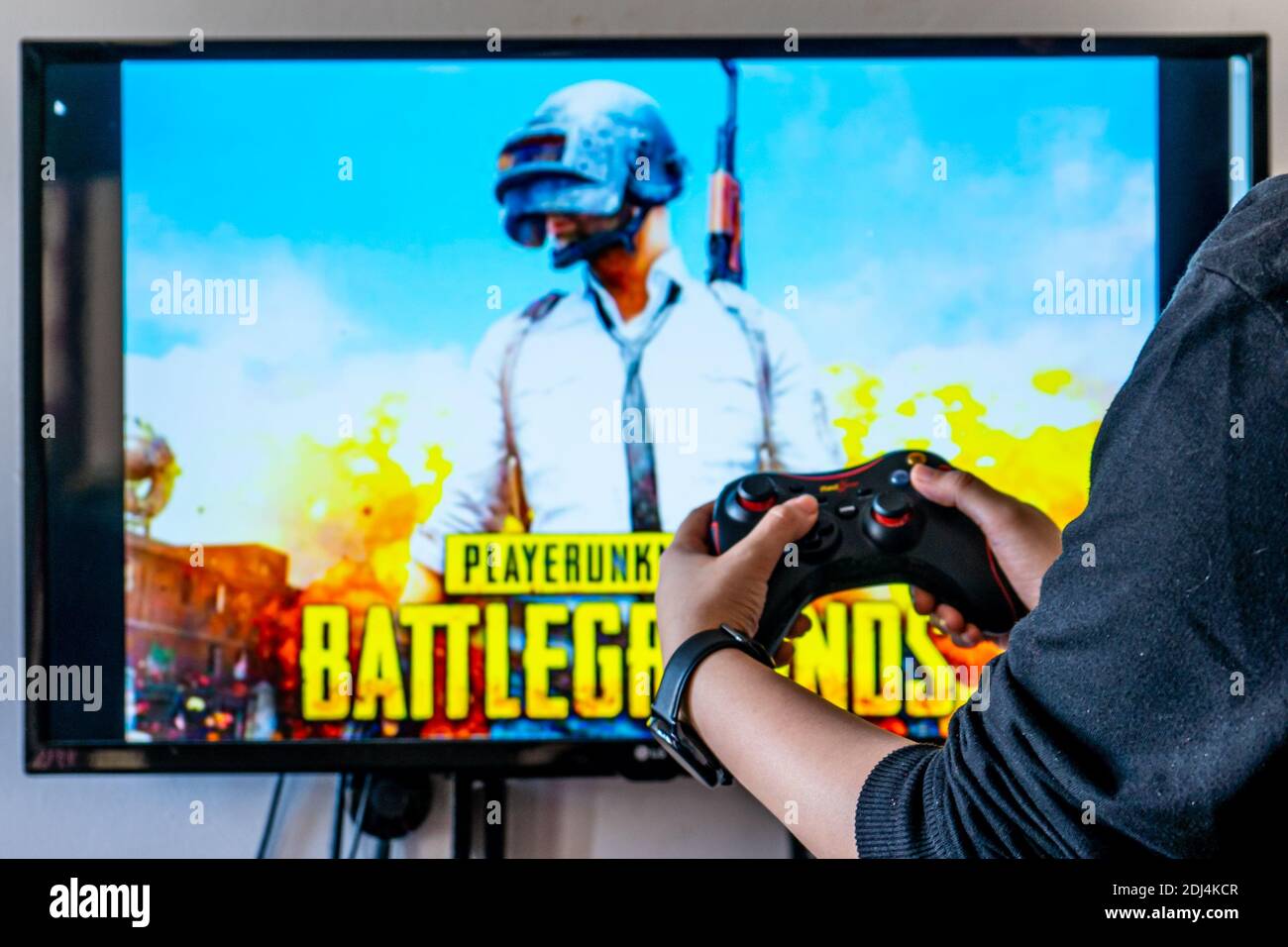 Woman holding a Generic controller and playing popular video game Player Unknown's battlegrounds PUBG on a television and PC Stock Photo