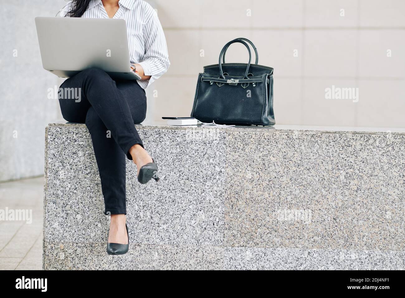 Cropped image of young female entrepreneur sitting outdoors next to her bag and worrking on laptop Stock Photo