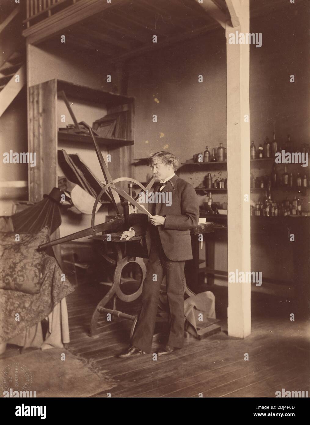 Whistler Standing at a Press in His Paris (rue Notre-Dame-des-Champs) Studio, Paul François Arnold Cardon, called 'Dornac', 1859–1941, French, 1893, Albumen print, Sheet: 10 1/4 x 8 inches (26 x 20.3 cm), artist, beam (structural element), blankets, bookcase, bottles, coat, collar, floorboards, man, painter, paper, pillow, portrait, printing press, printmaker, rafters, railing, rug, stairs, studio (work space), tie, top hat, trousers, vest, Europe, France, Paris Stock Photo