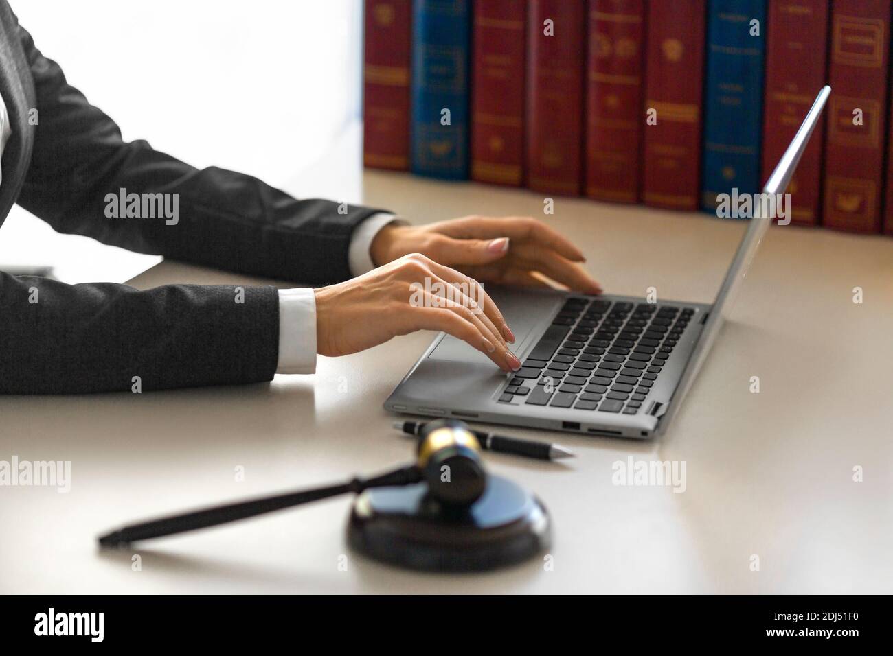 Female hands with a judge's gavel in front of a laptop monitor. Lawyer's office. Stock Photo