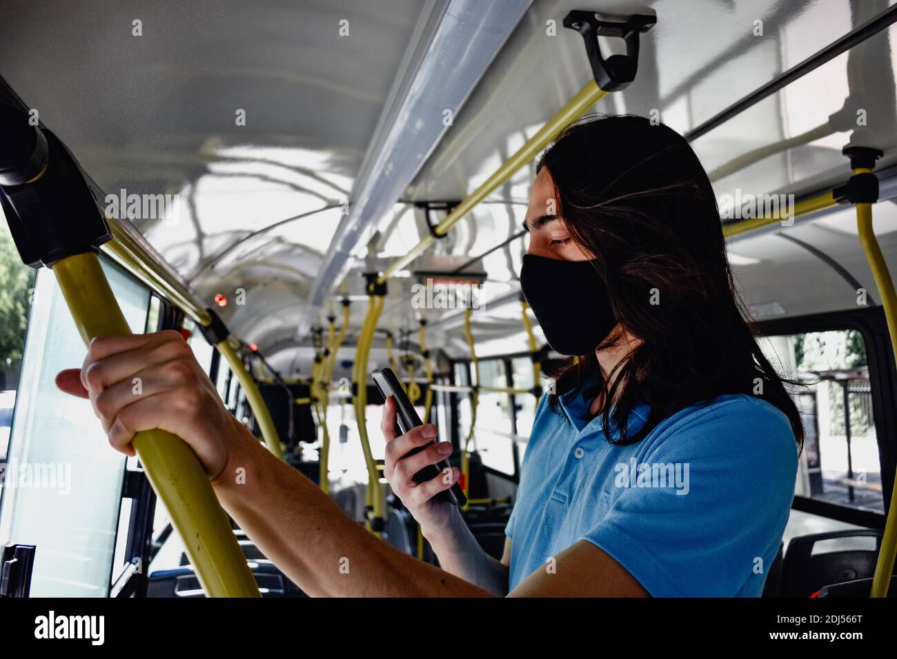 A man holds the handrail in the bus using phone wearing face mask Stock