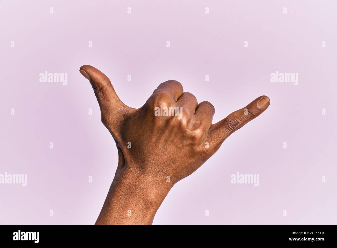 Arm and hand of black middle age woman over pink isolated background gesturing hawaiian shaka greeting gesture, telephone and communication symbol Stock Photo