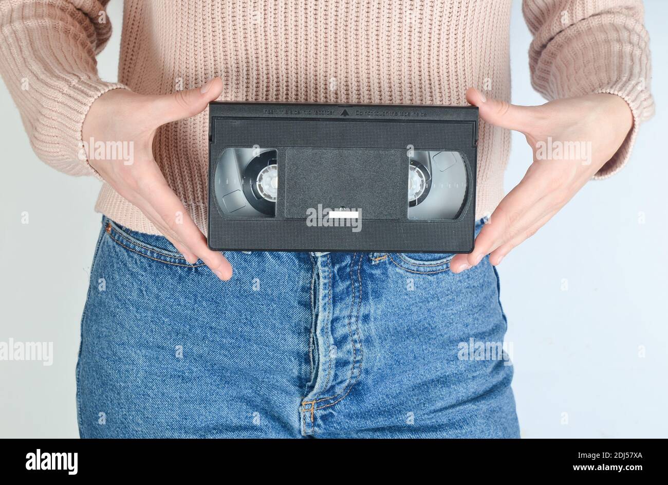 A girl in jeans holds a retro video cassette in hands on a white