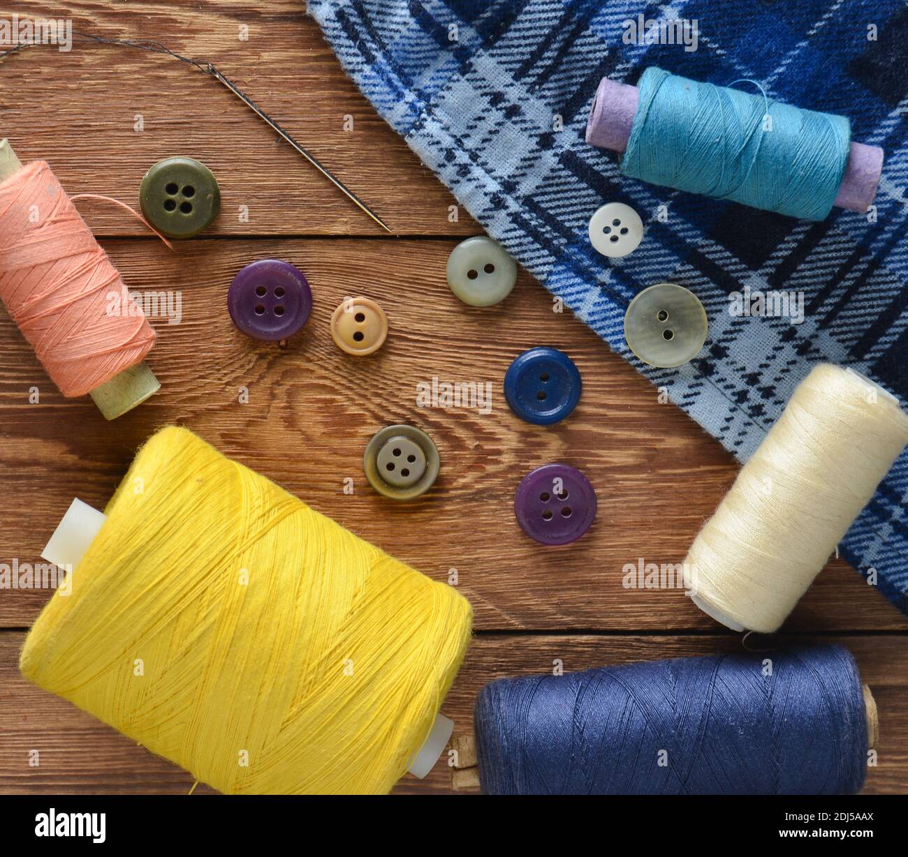 Colored threads, buttons, a needle on a wooden table. Objects for sewing. Top view. Stock Photo