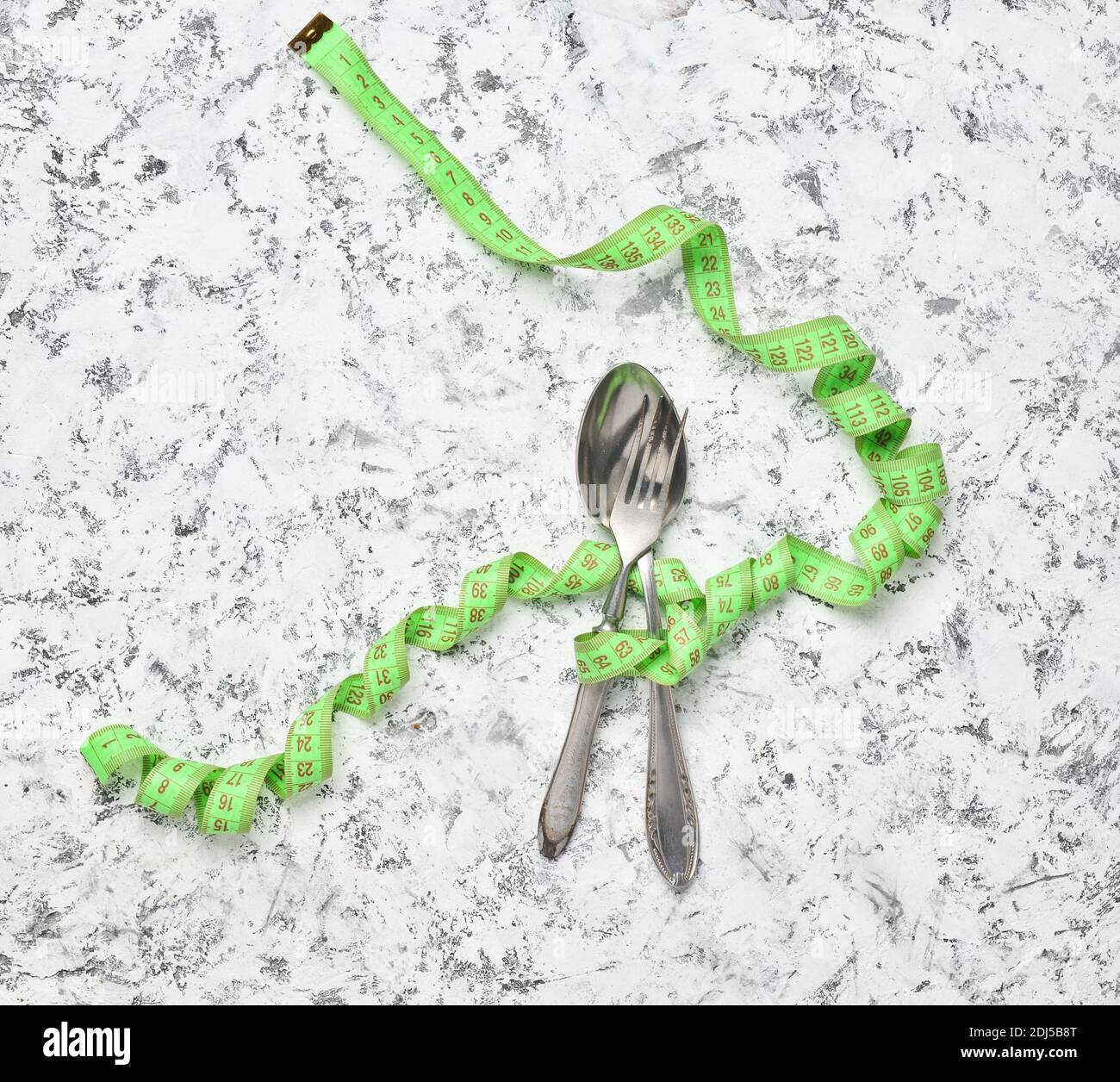 A metal spoon and fork wrapped with a ruler on a white concrete ...