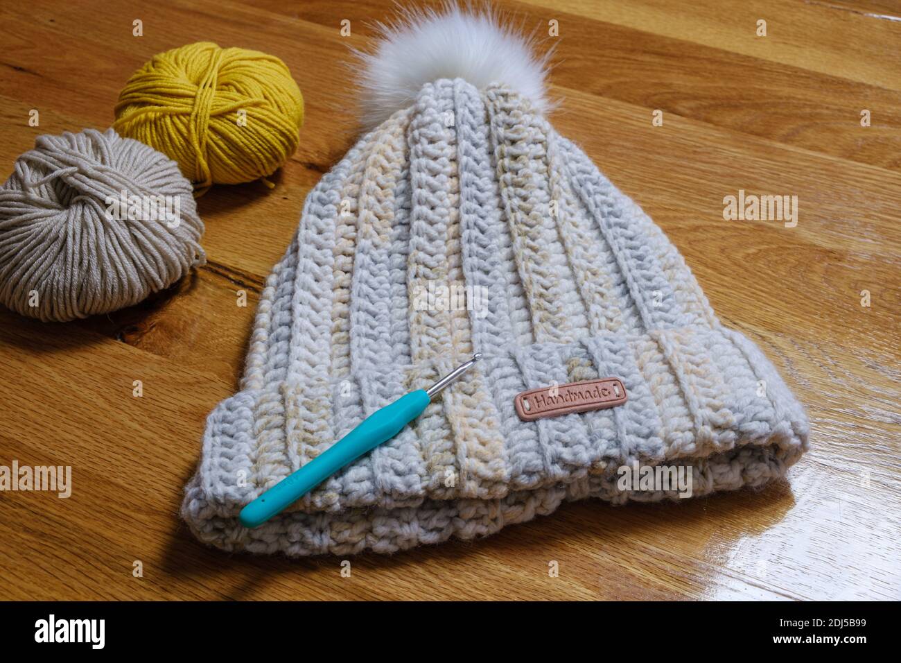 Handmade wool bobble hat on a wooden table with crochet hook and ball of wool. Stock Photo