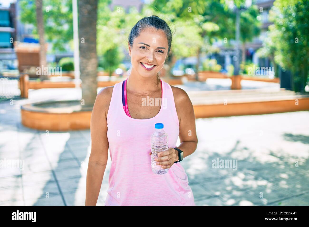 Middle age sportswoman smiling happy holding bottle of water at the ...