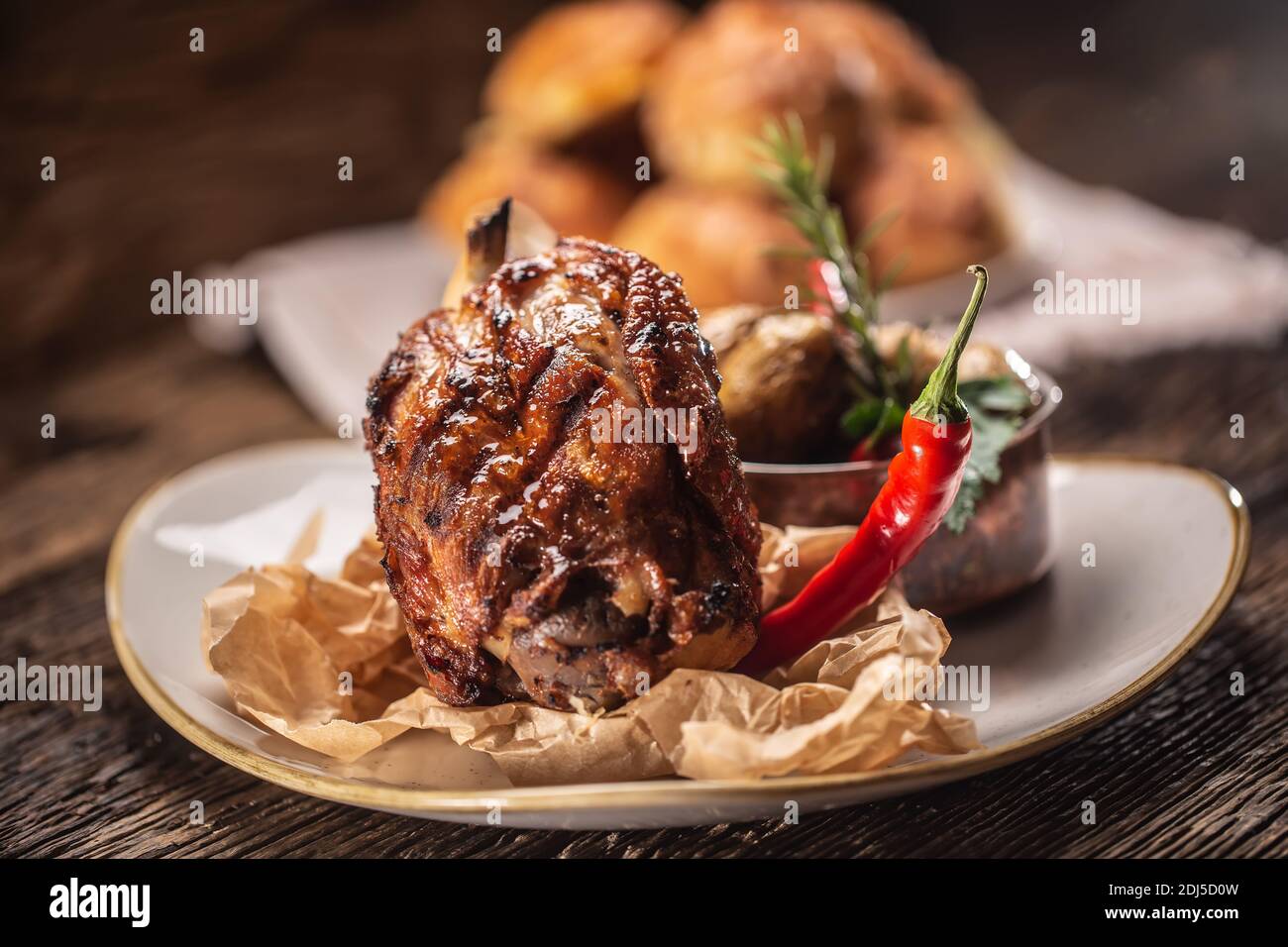 Ham hock baked with potatoes and served with a chilli with a rustic wooden background. Stock Photo