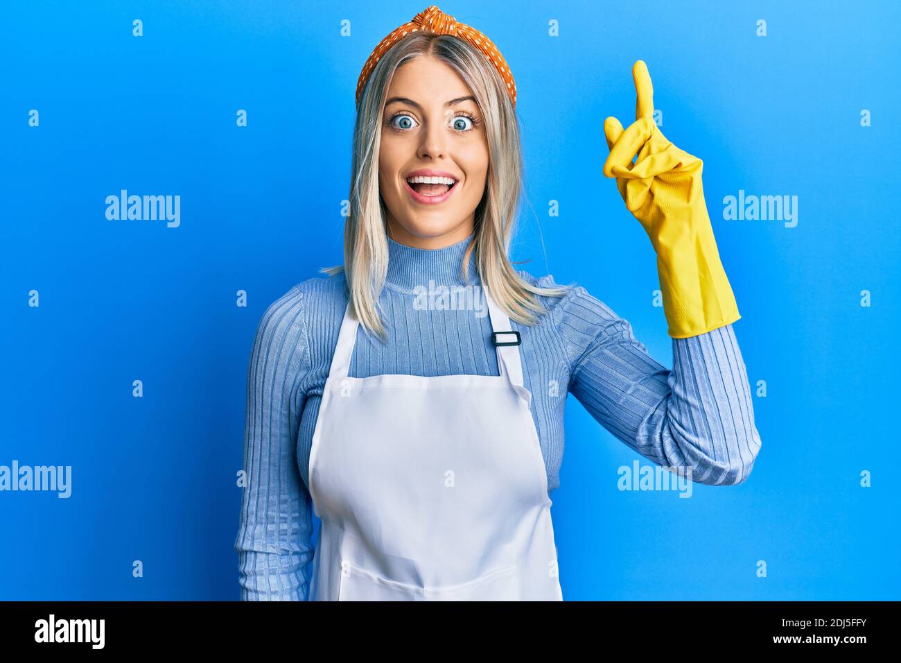 Beautiful blonde woman wearing cleaner apron and gloves pointing finger ...