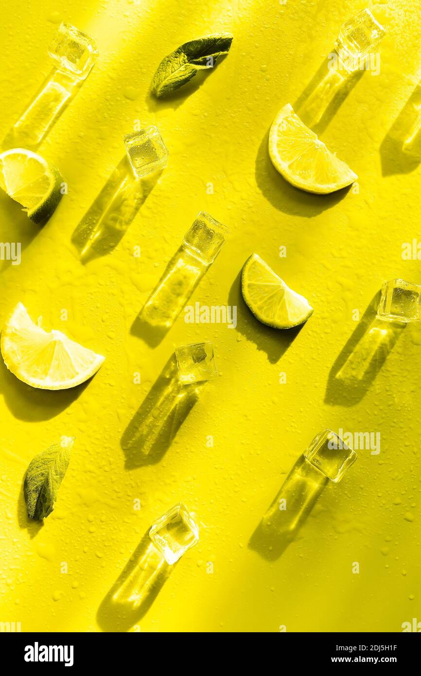Fresh mint leaf and ice cubes with droplets and lime on illuminating yellow background. Summer background Stock Photo