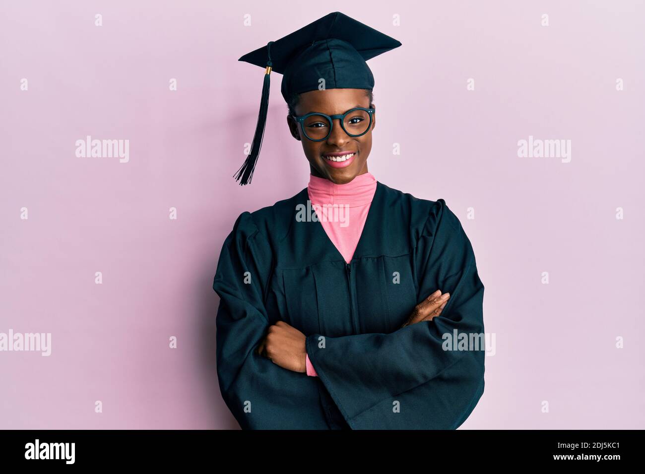 Young african american girl wearing graduation cap and ceremony robe happy face smiling with crossed arms looking at the camera. positive person. Stock Photo