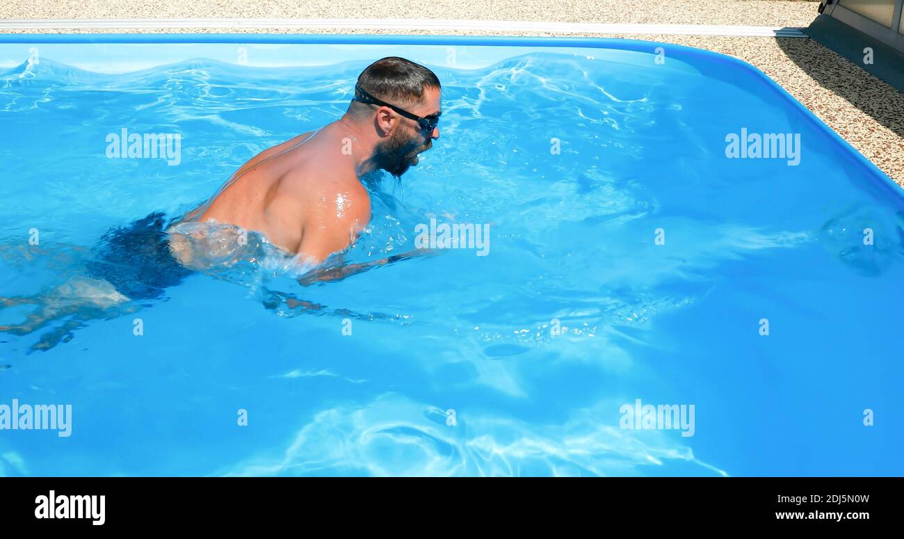 A young man trains in a home pool. Athlete swims in countercurrent ...