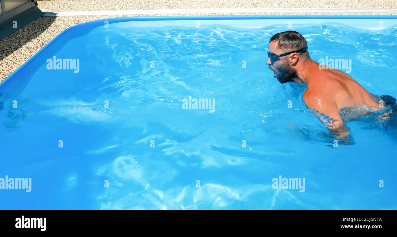 A young man trains in a home pool. Athlete swims in countercurrent ...