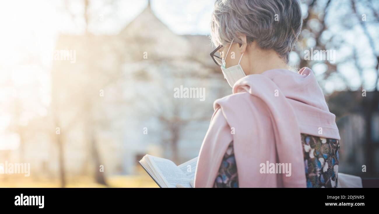 Senior lady with face mask reading the bible in front of a church Stock Photo