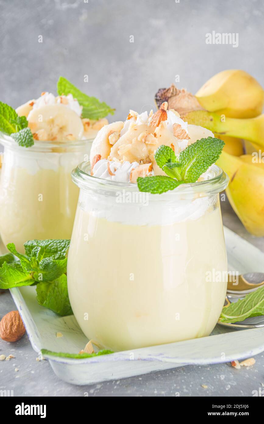 Fresh banana pudding for breakfast, banana yogurt. Sweet dessert in glasses with banana slices and nuts, raw vegetarian snack, on grey concrete backgr Stock Photo
