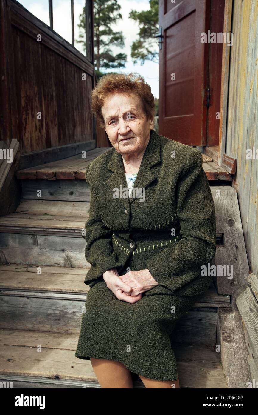 An old woman ninety years old, sitting on the porch of a village house ...