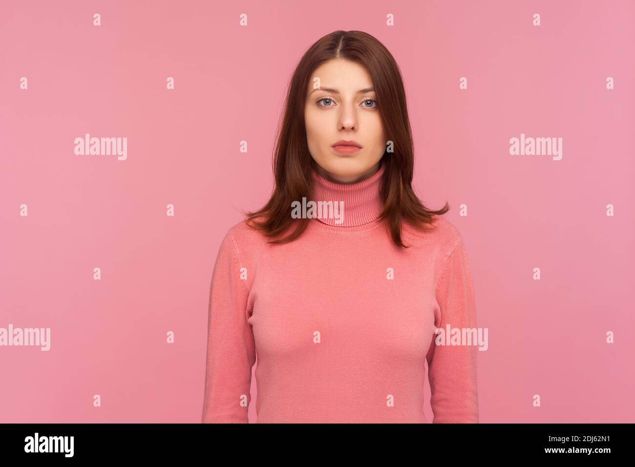 Portrait of serious self assured brunette woman looking at camera with confidence, sensuality and femininity. Indoor studio shot isolated on pink back Stock Photo