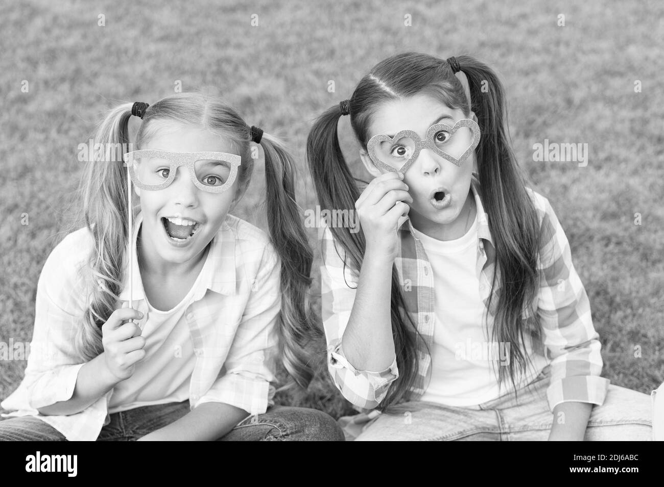 Looking fancy. Party girls wear prop glasses on green grass. Playful friends. Happy childhood. Fashion and beauty. Carnival fashion accessories. Summer fashion. Fashion style. Accessorize your look. Stock Photo