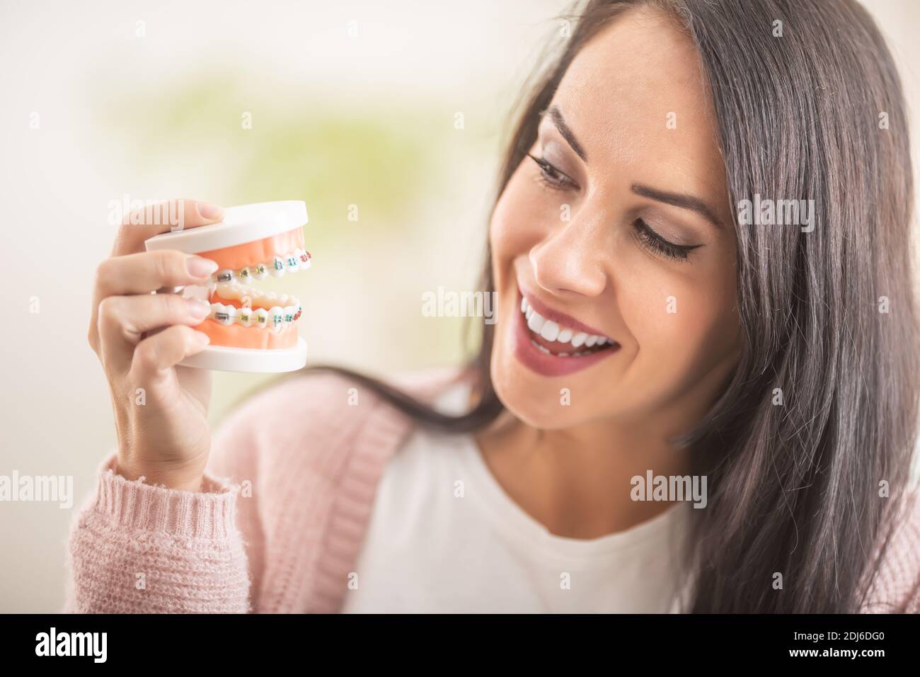 Smiling female looks at the colorful braces on teeth prothesis in her hand. Stock Photo