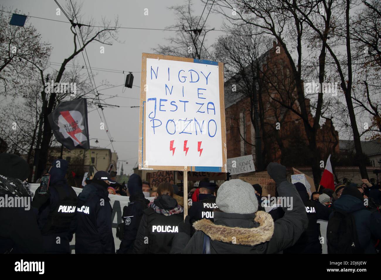 Krakow, Poland - December 13 2020: girl protest with banner NEVER IS TOO LATE in polish, red lightning, police tries to stop marching protesters Stock Photo