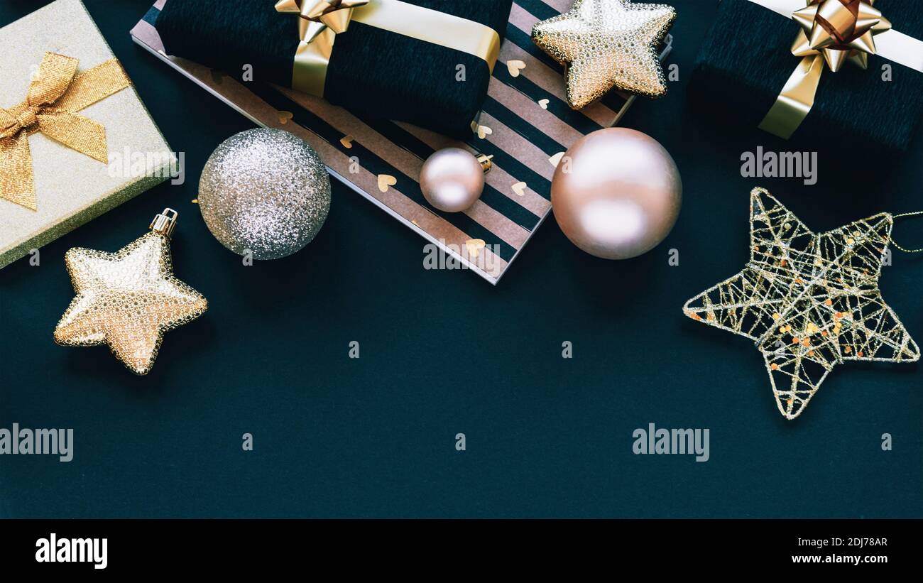 New Year gifts in black and golden boxes and Christmas toys on black background. Top view, flat lay, copy space. Stock Photo