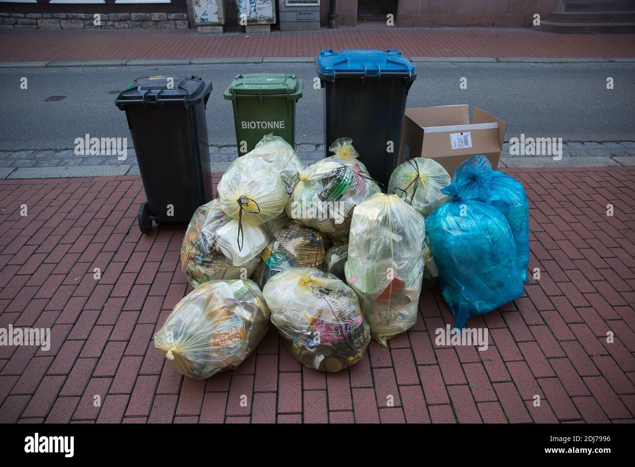 Plastic garbage bags and bins with recycling on paved sidewalk. Front view. Stock Photo