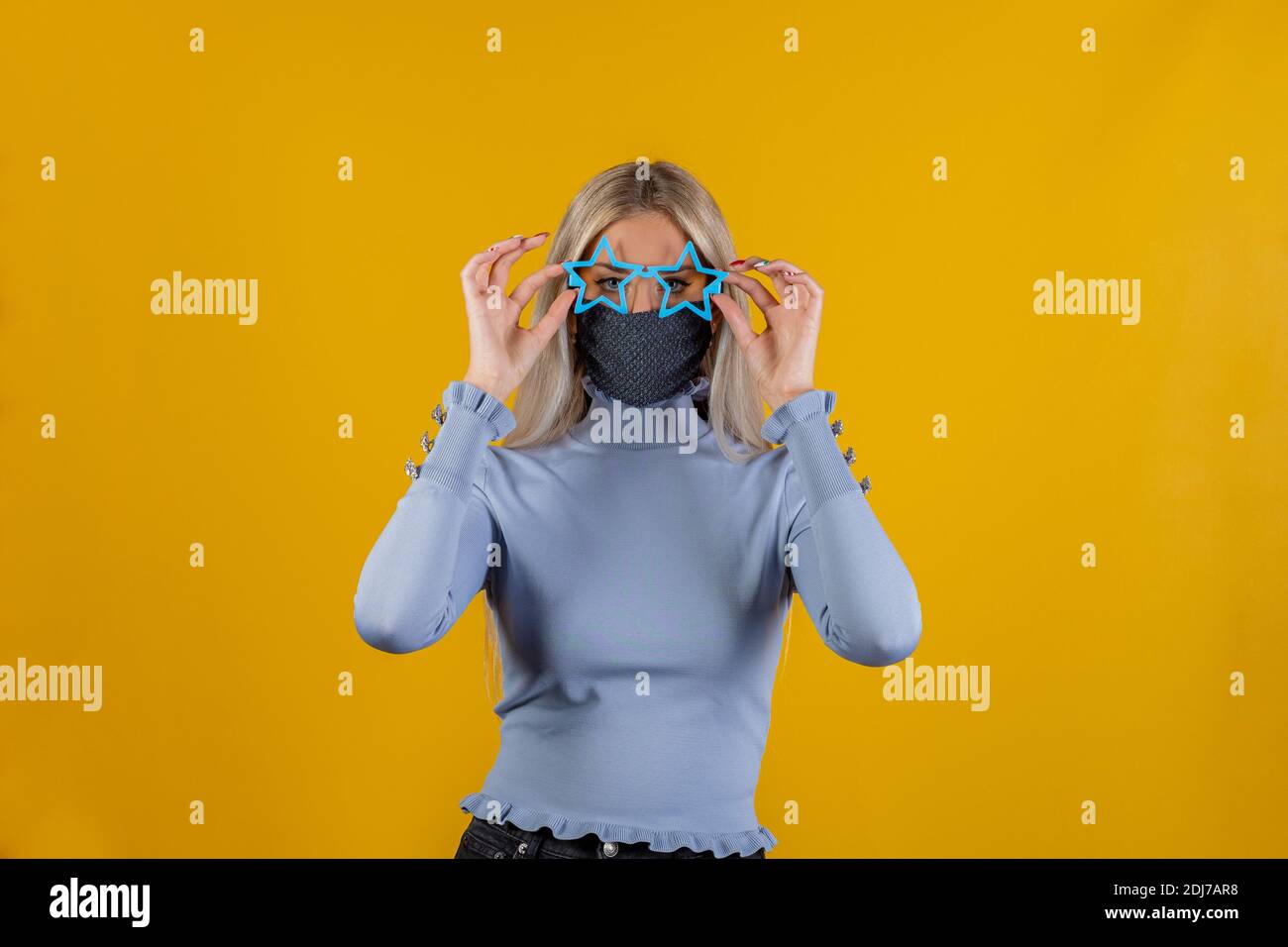 Portrait of funny pretty young woman wearing medical mask and funny glasses on yellow background. Conceptual photo of symbolizing the epidemic of the Stock Photo