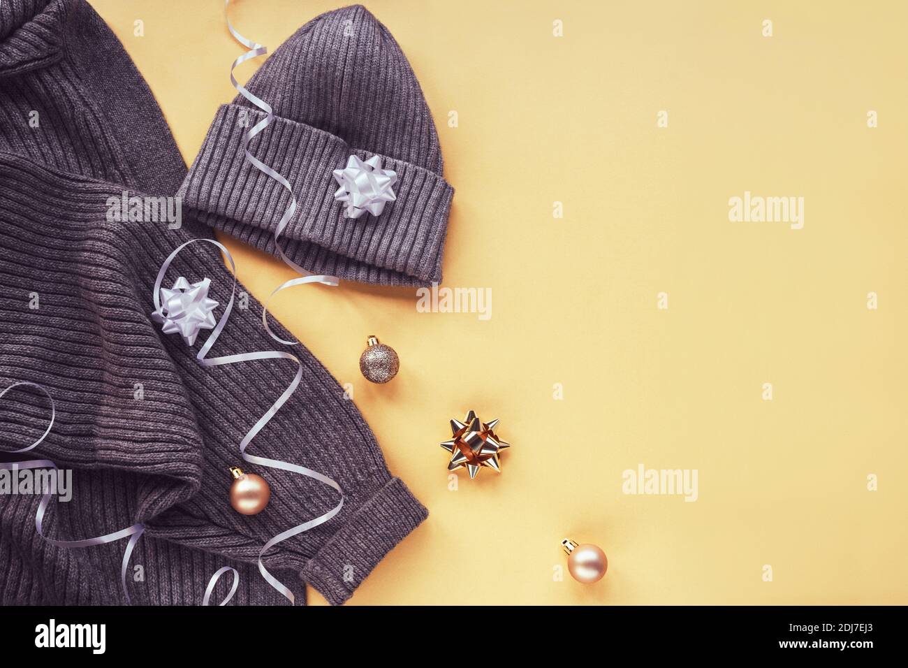 Gray cardigan sweater and cap on yellow background with baubles and tinsel. Winter holidays concept. Top view, flat lay. Stock Photo