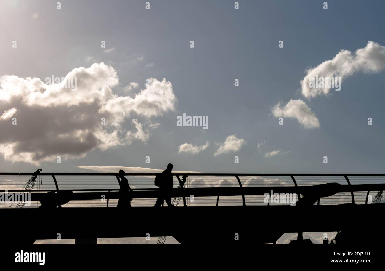 Millennium Bridge London with pedestrians silhouetted against a blue sky with an aircraft contrail Stock Photo