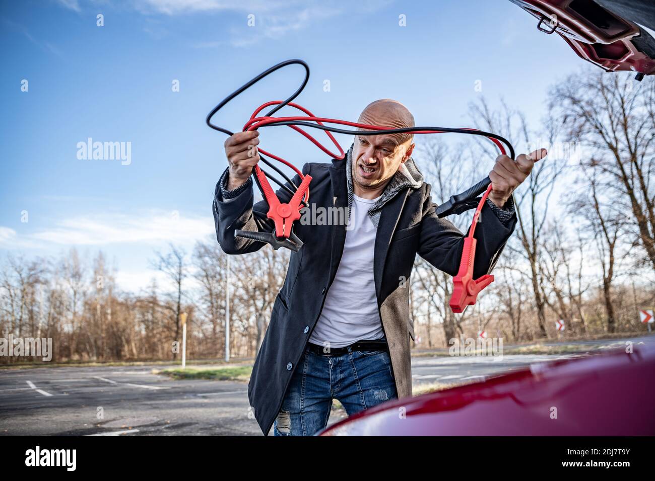 Angry driver trying to start broken car with jumper cables Stock Photo