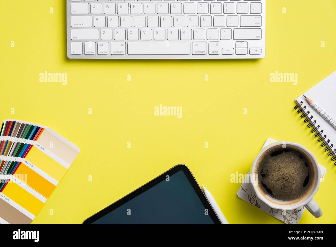 Professional creative graphic designer desk with computer keyboard, tablet, color palette, cup of coffee, notebook on yellow background. Flat lay, top Stock Photo